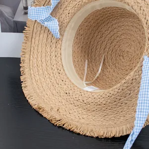 Flat top straw sun hat with blue gingham ribbon and frayed edges for beach vacations