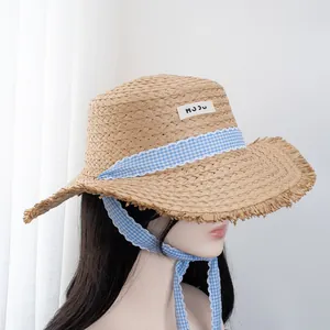 Detail of wide brim straw hat with blue plaid ribbon and delicate lace trim