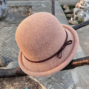 Close-up of a woven cloche hat with a bow detail hanging on a tree branch in a garden