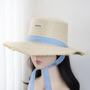 Detail of flat top straw hat with blue gingham ribbon and frayed edge design