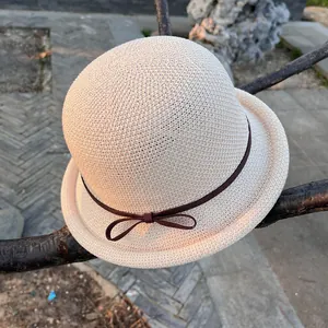 Close-up of beige woven sun hat with brown ribbon bow hanging on a natural tree branch