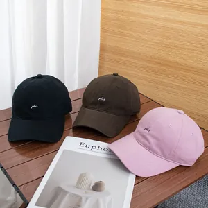 Drie geborduurde katoenen baseballcaps in zwart, bruin en roze op een houten buitentafel