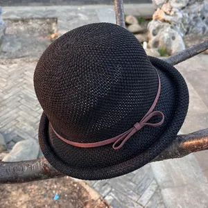 Detailed view of black knitted cloche hat with a brown bow ribbon on a tree branch