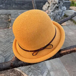 Detail of yellow knit bucket hat with brown ribbon bow on a tree branch outdoors