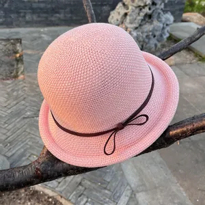 Close-up of pink knitted sun hat with a brown ribbon bow hanging on a branch