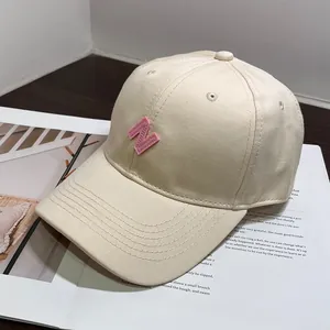 Detalle de gorra de béisbol crema con bordado de letra N rosa en lona de algodón