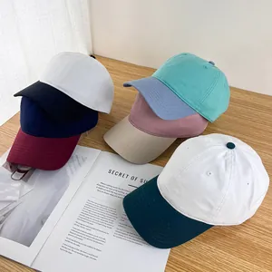 Assorted cotton baseball caps in multiple colors stacked on a wooden table with a magazine