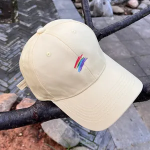 Detalle de gorra de algodón amarillo claro con bordado de arcoíris en una rama