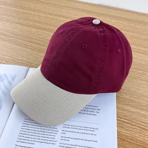 Detail view of contrast baseball cap with burgundy crown and beige brim on wooden desk