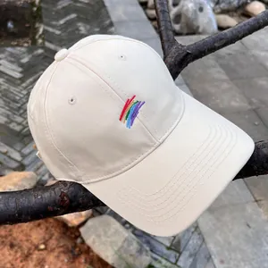 Detalle de gorra de algodón beige con bordado de arcoíris sobre una rama de árbol