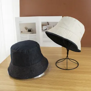 Reversible blue denim sun hat and cream bucket hat displayed on a modern metal stand