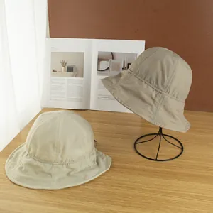 Primer plano de sombreros de sol plegables en beige y gris claro sobre mesa de madera