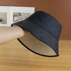 Detail of reversible blue denim bucket hat featuring white contrast stitching and brown lining