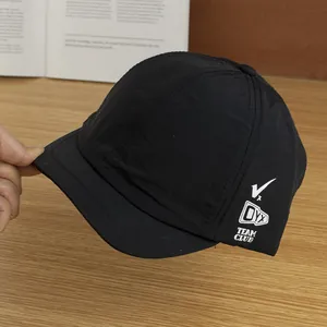 Detail van de ademende nylon stof en witte zijbelettering op een zwarte pet met korte klep