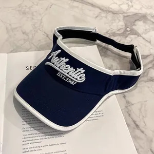 Dettaglio visiera parasole blu navy con ricamo 3D bianco su tavolo di marmo