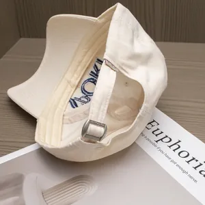 Back view of cream cotton baseball cap with silver metal buckle on wooden desk