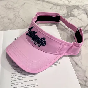 Dettaglio visiera parasole rosa con ricamo blu su sfondo di rivista e marmo grigio