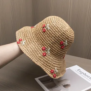 Detail of hand-woven straw hat featuring vibrant red cherry embroidery for summer travel