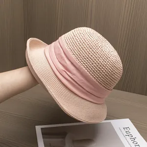 Détail du chapeau de paille rose avec ruban plissé élégant sur fond de bois naturel
