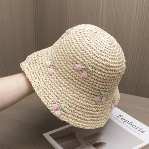 Close-up of beige straw sun hat featuring pink cherry embroidery and crochet texture
