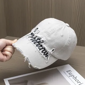 Dettaglio del cappellino ricamato con bordi sfilacciati, effetto usurato e cotone lavato
