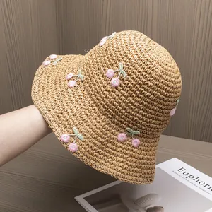 Close-up of straw sun hat with delicate pink cherry embroidery and woven texture detail
