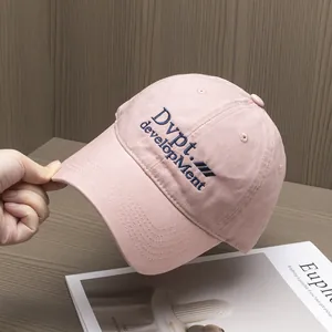 Détail de casquette rose en coton avec broderie bleue sur un fond en bois naturel