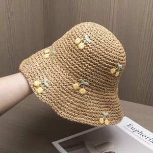 Close-up of handmade straw hat featuring yellow cherry embroidery and crochet texture