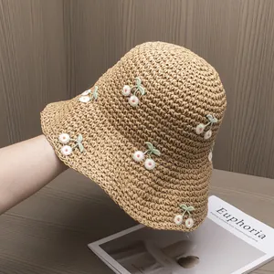 Close-up of hand-woven straw hat featuring delicate cherry embroidery and wavy brim