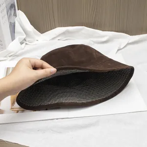 Detail of dark brown suede bucket hat with black and white plaid lining on soft background