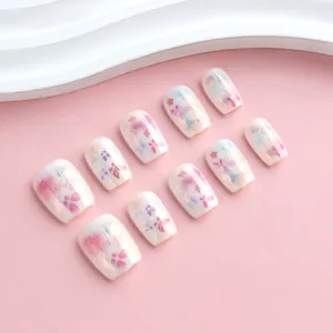 Floral press-on nails with purple flower art and gold leaf accents on a pink background