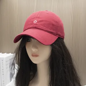 Detailed view of a dark red cotton baseball cap with white embroidery on a light wood background