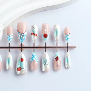 Detail of almond-shaped press-on nails featuring relief cherries and blue grid patterns