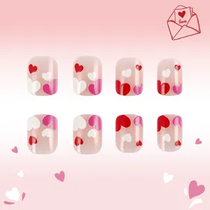 Detail of short square press-on nails featuring red and pink heart patterns and glitter