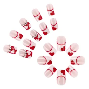 Glossy short press-on nails with red heart patterns and sparkling rhinestone accents