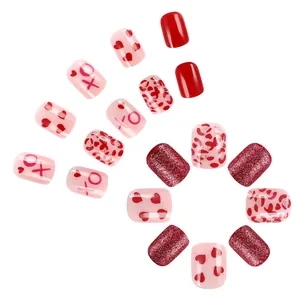 Short square press-on nails with red hearts, glitter, and XO patterns in pink and red tones