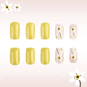 Detailed view of yellow press-on nails with white floral patterns and glossy finish