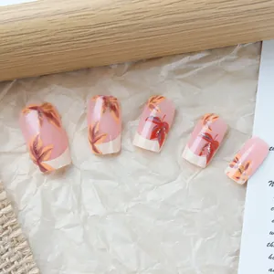 Macro detail of French press-on nails featuring autumn maple leaf designs and gold glitter