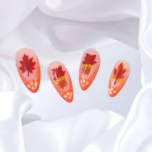 Macro detail of almond press-on nails featuring orange autumn maple leaf designs