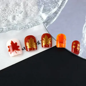 Vista detallada de uñas postizas otoñales con patrones de hojas de maple rojas y oro