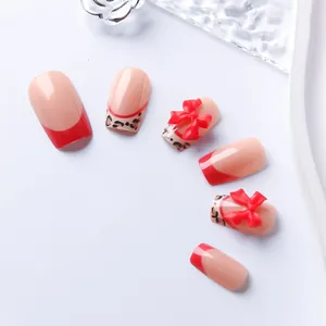 Macro detail of red French tip press-on nails with leopard patterns and 3D bow accents