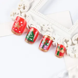 Close-up of red Christmas press-on nails with tree patterns and gold glitter accents