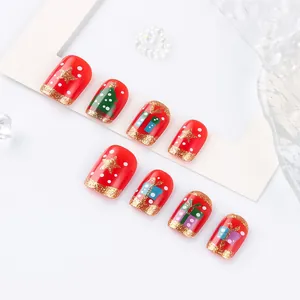 Detail of red Christmas press-on nails featuring gold glitter, trees, and star patterns