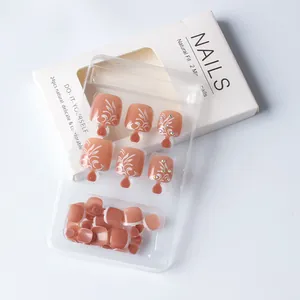 Detail of nude pink press-on toe nails with white floral patterns and sparkling rhinestones