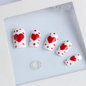 Detail of white square press-on nails featuring red heart and polka dot patterns