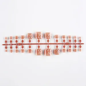 Detail of 24 French style nude pink press-on toe nails with white floral patterns and rhinestones