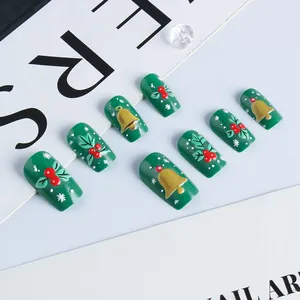 Détail de faux ongles de Noël verts avec motifs en relief de cloches et de cerises de fête