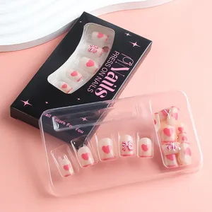 Detail of short press-on nails with 3D bows and heart patterns in elegant black packaging