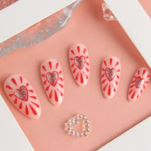 Detail of almond nails with red glitter hearts and radiant droplet designs on pink base