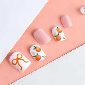 Close-up of pink press-on nails with peach motifs and orange bows on a split background